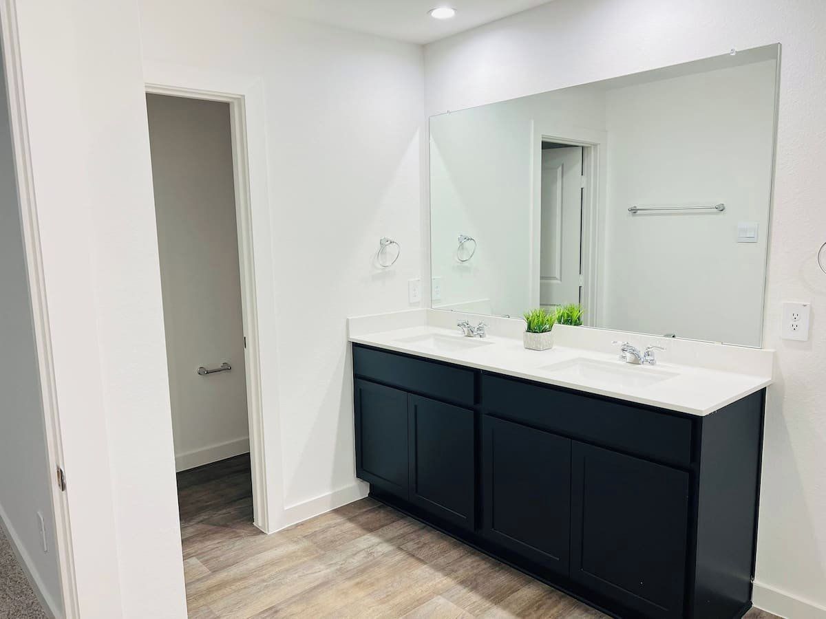 A modern bathroom with a double sink vanity, a large mirror, and a door leading to another room.