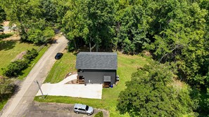A single-story building with a dark roof, surrounded by dense greenery and a paved driveway. - Honey's Hideaway I An Exclusive TN River Retreat! (Birchwood)
