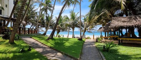 A pathway leading to a beach with palm trees and a thatched structure.