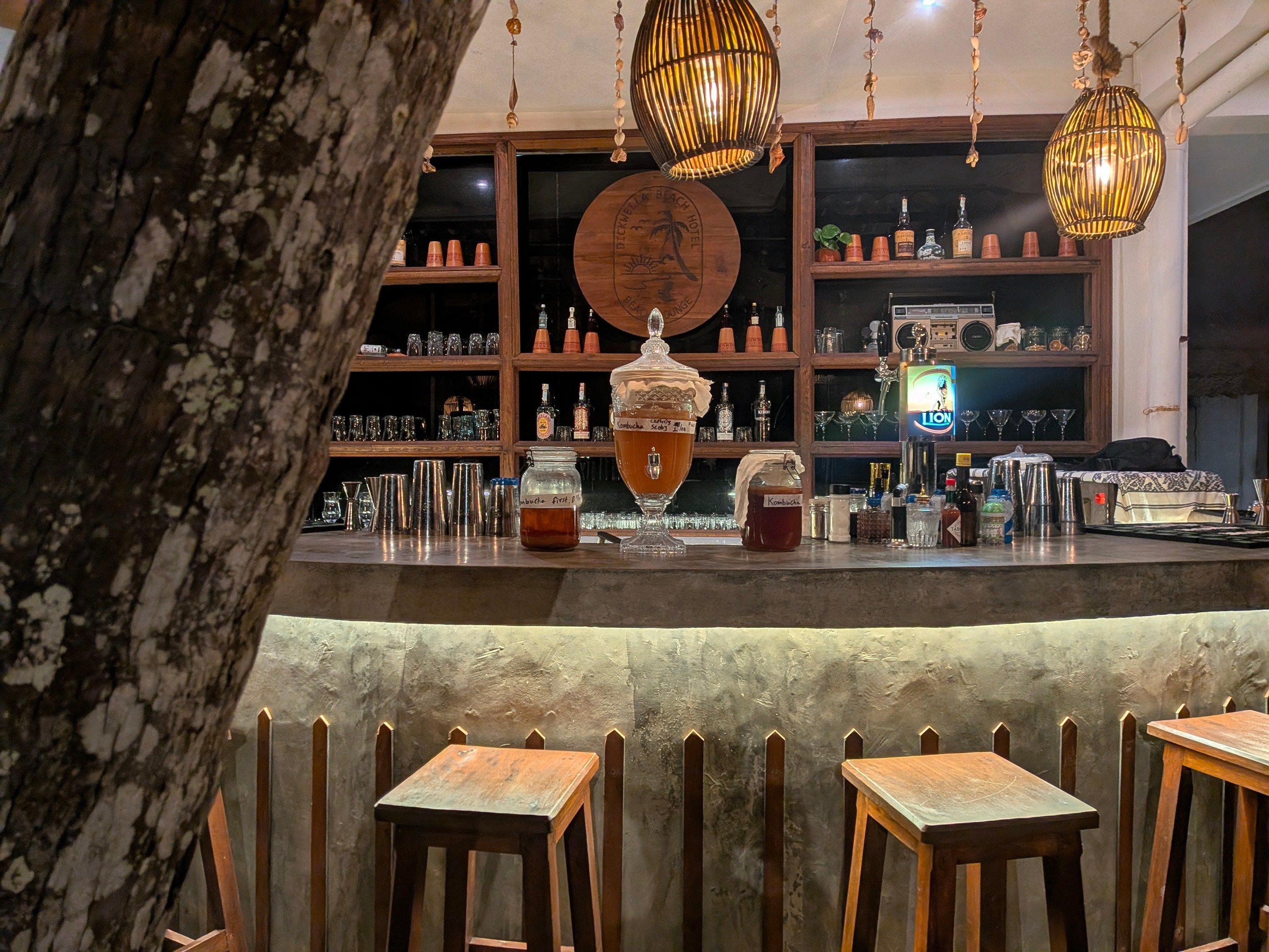 Una zona de bar con estantes de madera, mostrador y luces colgantes.