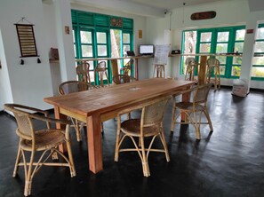Una habitación con una larga mesa de madera rodeada de sillas de mimbre, una pizarra y una computadora en un escritorio.