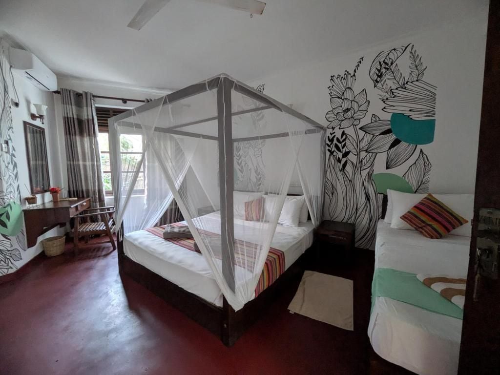 A room with a bed under a mosquito net, a desk with a chair, and a wall with a floral mural.