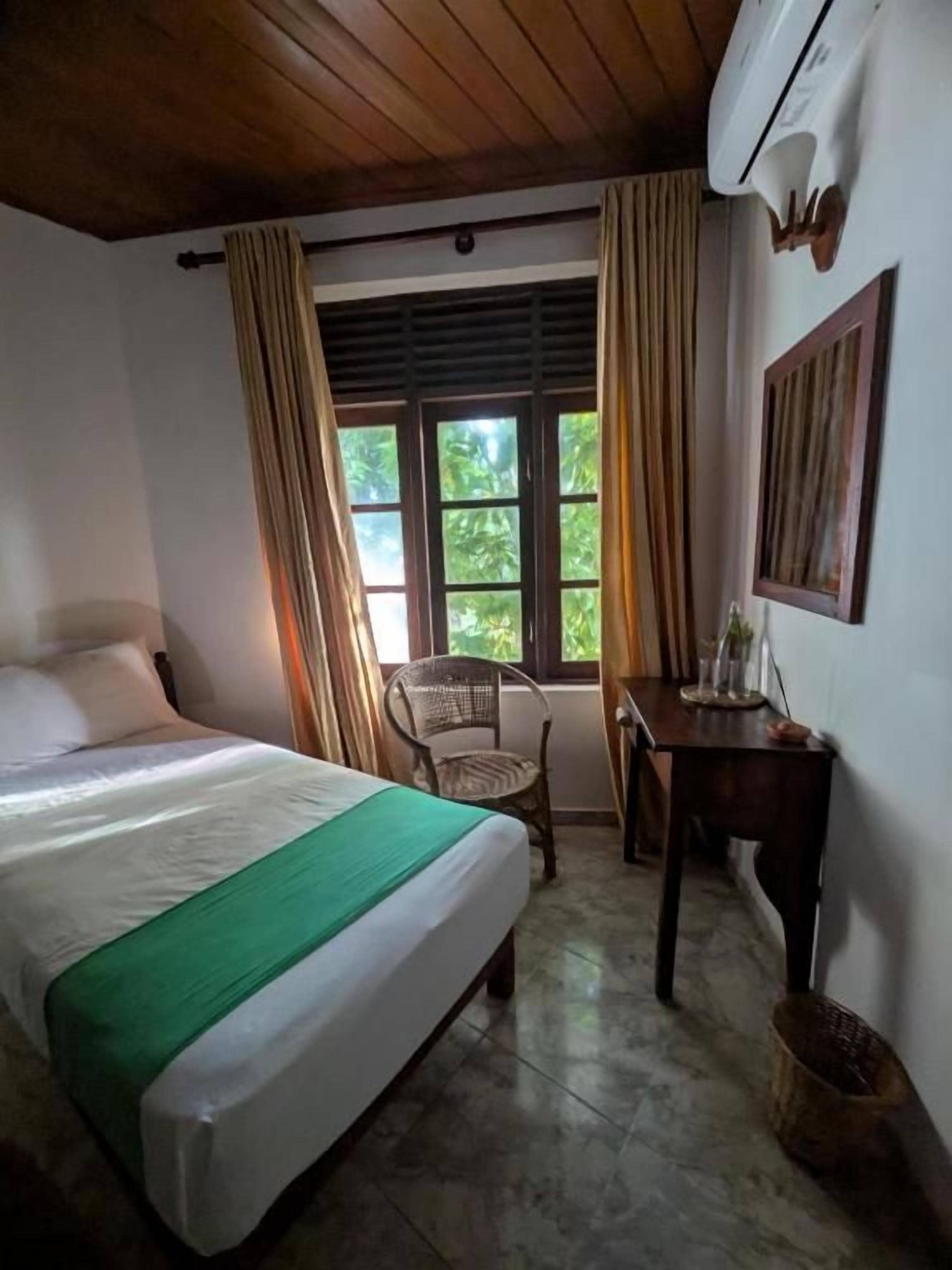 A room with a bed, a chair, a table, and a window with curtains.