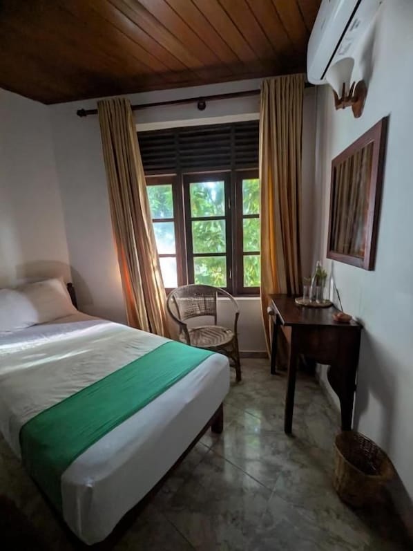 A room with a bed, a chair, a table, and a window with curtains.