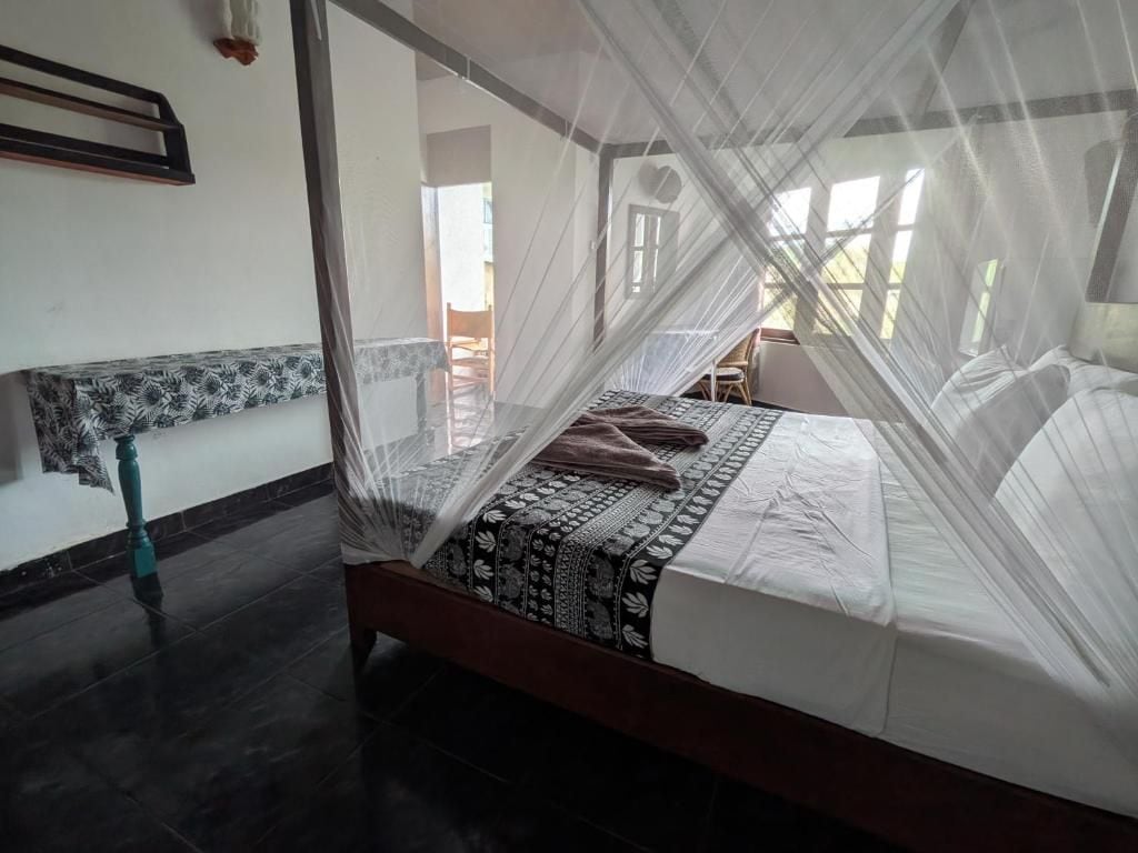 Una cama con mosquitero, una colcha estampada y vistas al exterior a través de una ventana.