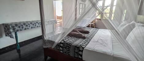 Una cama con mosquitero, una colcha estampada y vistas al exterior a través de una ventana.
