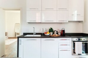Une cuisine moderne avec des meubles blancs, un plan de travail noir, un évier, une cuisinière et une machine à café.