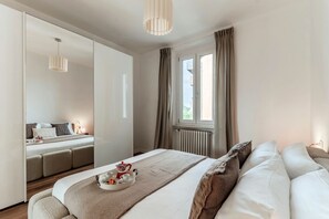 A modern bedroom with a large bed, a bedside table with a tray of breakfast items, a mirror, and a window with curtains. - Como In The Sky - 150 steps, by MyHomeInComo (Como)