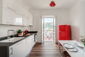 A modern kitchen with white cabinets, a red refrigerator, and a dining area with a table set for two. - Como In The Sky - 150 steps, by MyHomeInComo (Como)