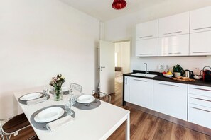 Une cuisine moderne avec des meubles blancs, une table à manger pour quatre personnes et un luminaire suspendu rouge.