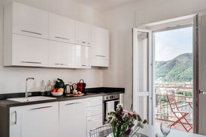 A modern kitchen with white cabinets, a black countertop, and a view of a balcony with a chair. - Como In The Sky - 150 steps, by MyHomeInComo (Como)