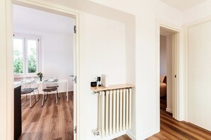 Une pièce avec un plancher en bois, un radiateur et une porte qui donne sur une autre pièce.