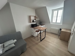 En kompakt opholdsstue med tekøkken, spiseplads, sofa og et vindue.