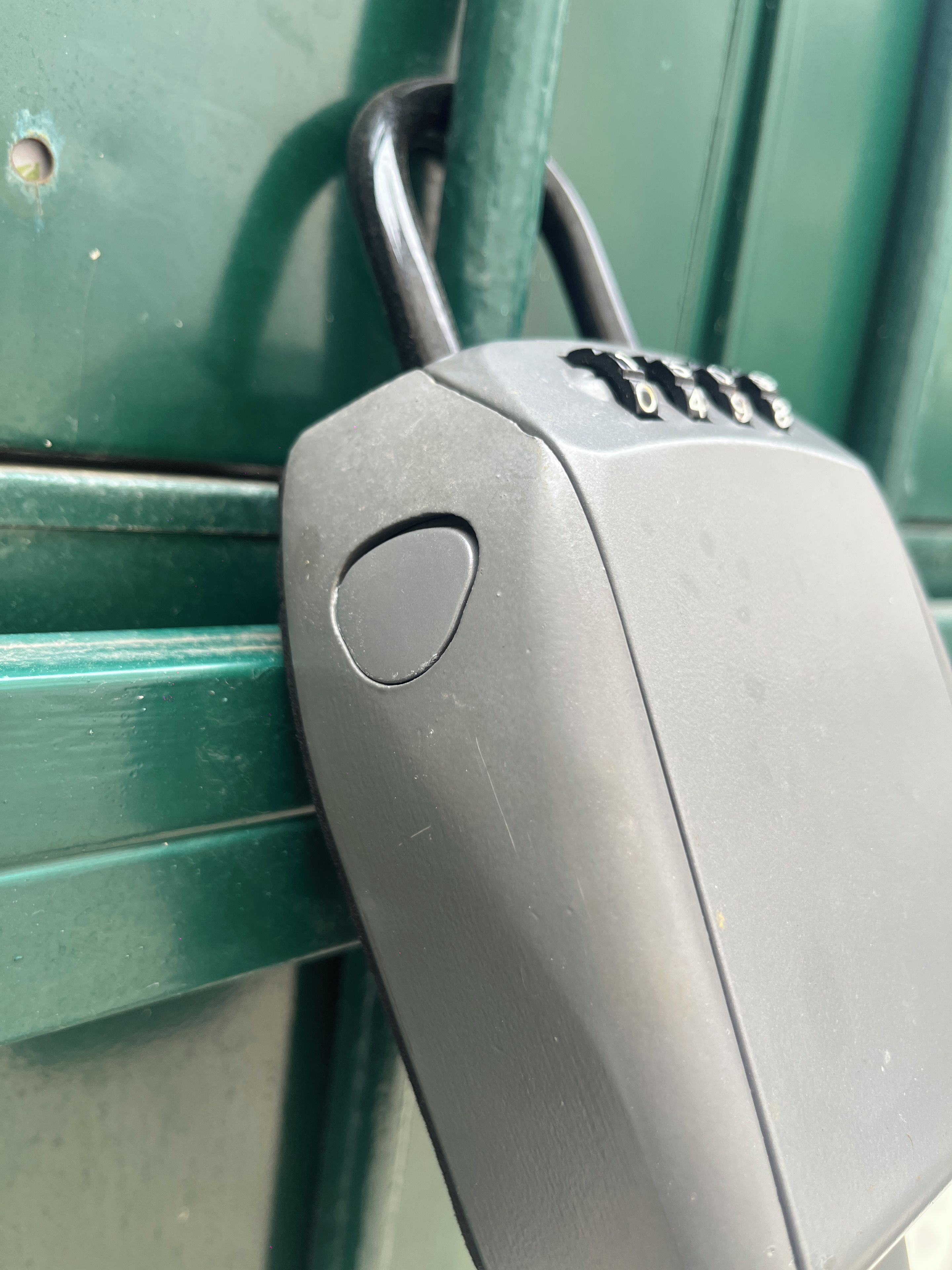 En metalkasse med et tastatur, muligvis en sikkerhedsanordning, fastgjort til en grøn metaloverflade.