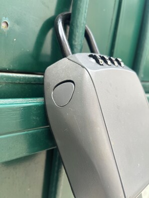 En metalkasse med et tastatur, muligvis en sikkerhedsanordning, fastgjort til en grøn metaloverflade.