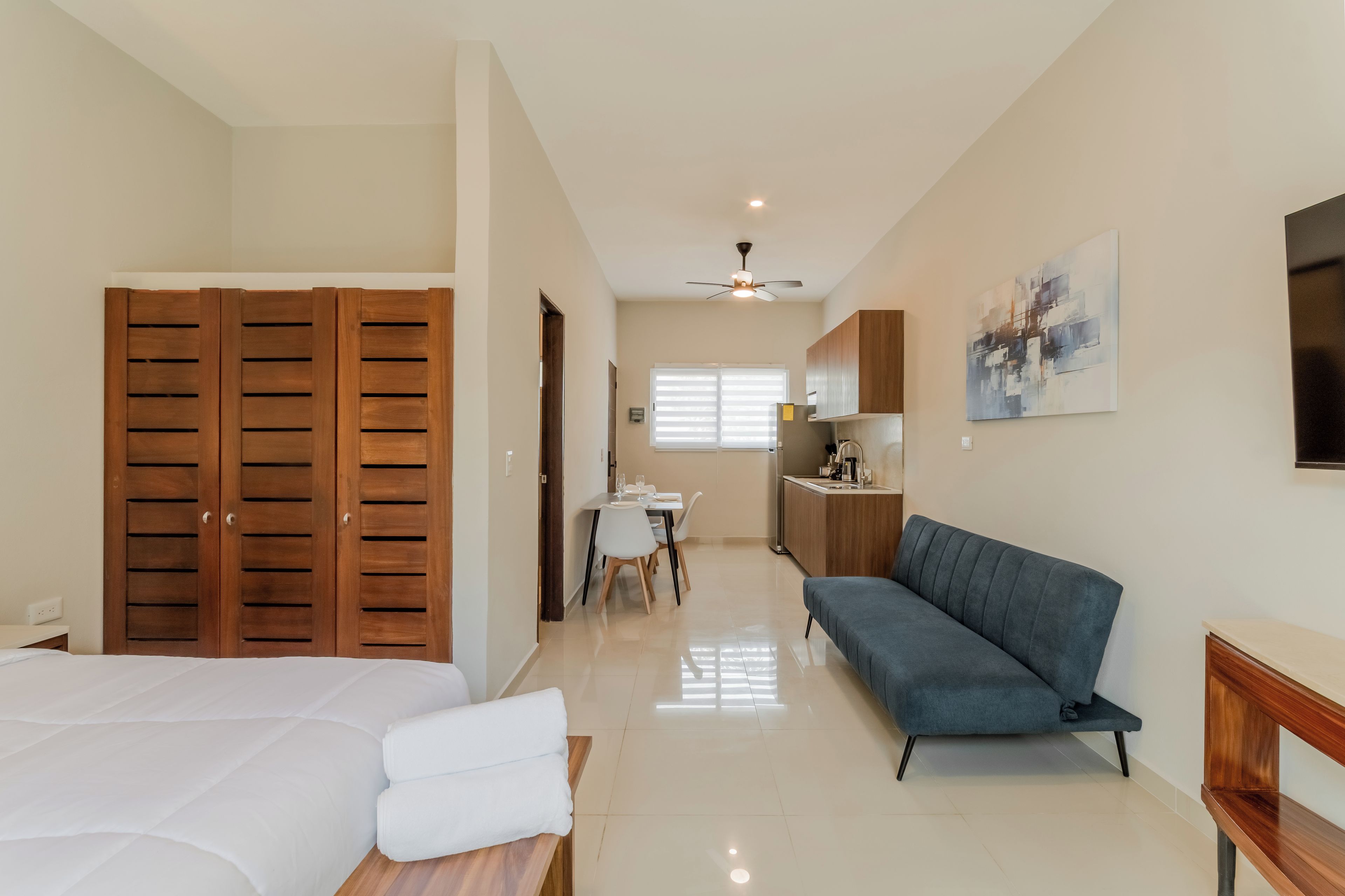A hotel room with a bed, a sofa, a dining area, and a kitchenette.