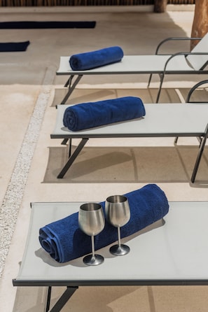 A row of sun loungers with blue towels and two wine glasses on one of them.