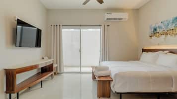 Quarto de hotel com cama, televisão, ventoinha no teto, ar condicionado, pintura e porta de vidro deslizante.