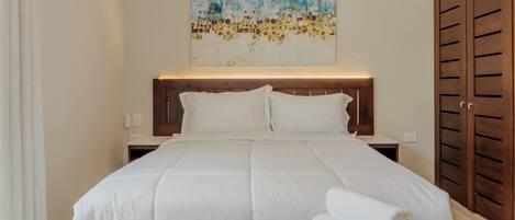 A hotel room with a bed, a headboard, a bedside table, a nightstand, a wooden wardrobe, and a wall-mounted artwork.