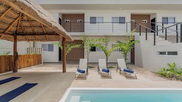 A pool area with lounge chairs and a thatched roof structure.