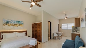 A hotel room with a bed, a desk, a chair, a bench, a ceiling fan, and a painting on the wall. - Brisa  (Cancún)