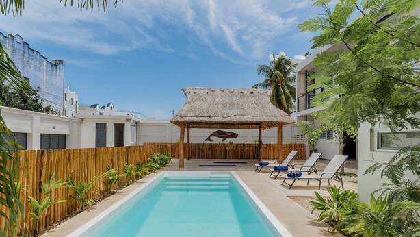 A swimming pool with lounge chairs and a thatched-roof gazebo. - Brisa  (Cancún)