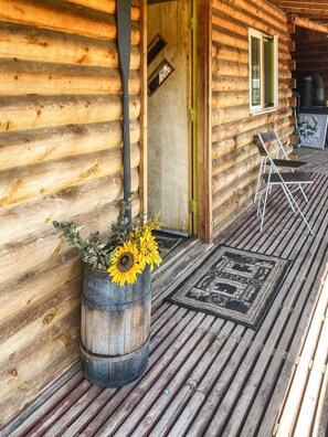 A log cabin with a wooden porch, a chair, and a potted plant with sunflowers.