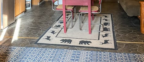 Interior rústico de una cabaña con una mesa de comedor de madera, sillas, un refrigerador y una zona de cocina.