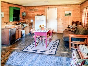A cozy cabin interior with a dining table, chairs, a sofa, and a kitchen area.