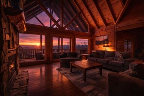 Ein gemütliches Blockhaus-Interieur mit Kamin, einer Sofagarnitur und einem großen Fenster mit herrlichem Ausblick.
