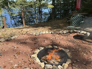 A fire pit surrounded by rocks, a chair, and a view of a lake. - Birch Tree Retreat - Cozy 2BR Lake Escape on Eco Lake (Eagle River)