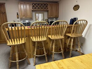 A kitchen with wooden cabinets, a microwave, and a bar area with four wooden bar stools. - Birch Tree Retreat - Cozy 2BR Lake Escape on Eco Lake (Eagle River)