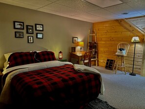A bedroom with a bed, a desk, a chair, and a wooden wall. - Birch Tree Retreat - Cozy 2BR Lake Escape on Eco Lake (Eagle River)