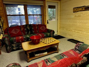 A cozy living room with a wooden sofa, a red bowl, and a Monopoly board game. - Birch Tree Retreat - Cozy 2BR Lake Escape on Eco Lake (Eagle River)
