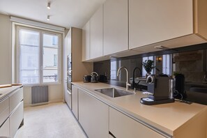 A modern kitchen with a large window, built-in appliances, and a stone accent wall. - Duplex in the center of Paris (Paris)