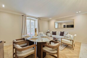 A dining area with a round table, wooden chairs, and a sofa in the background. - Elegant Apartment with AC - Center of Paris (Paris)