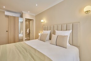 Une chambre d’hôtel avec un grand lit, une armoire en bois, une salle de bain avec une porte en verre et un luminaire fixé au mur.