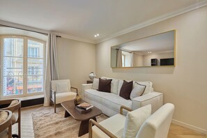 A modern living room with a white sofa, a coffee table, and a large mirror on the wall. - Elegant Apartment with AC - Center of Paris (Paris)