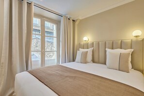 A hotel room with a large bed, two bedside lamps, a window with curtains, and a view of buildings outside. - Elegant Apartment with AC - Center of Paris (Paris)