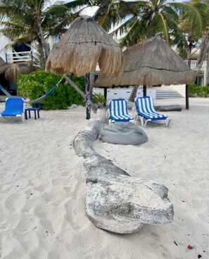 A sandy beach with thatched umbrellas, striped lounge chairs, and a large rock formation. - Villa Sunray. Entire 5 bedroom Villa with private pool and beach (Q.R.)