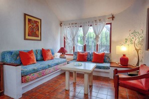 Uma sala de estar aconchegante com um sofá, uma mesa de centro e uma poltrona. Há um quadro na parede e um abajur sobre a mesa.