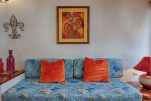 Una habitación con una cama, dos almohadas naranjas, una obra de arte enmarcada y una lámpara roja.