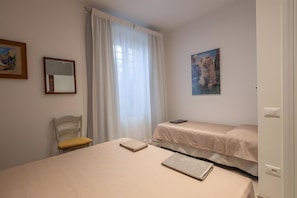 Une chambre à coucher avec un lit, une chaise, un tableau et une fenêtre avec des rideaux.
