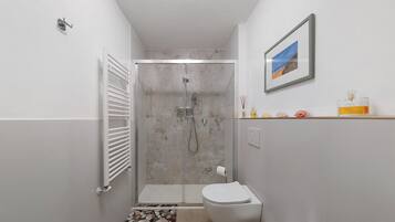 A bathroom with a glass-enclosed shower, a toilet, and a small shelf with toiletries.