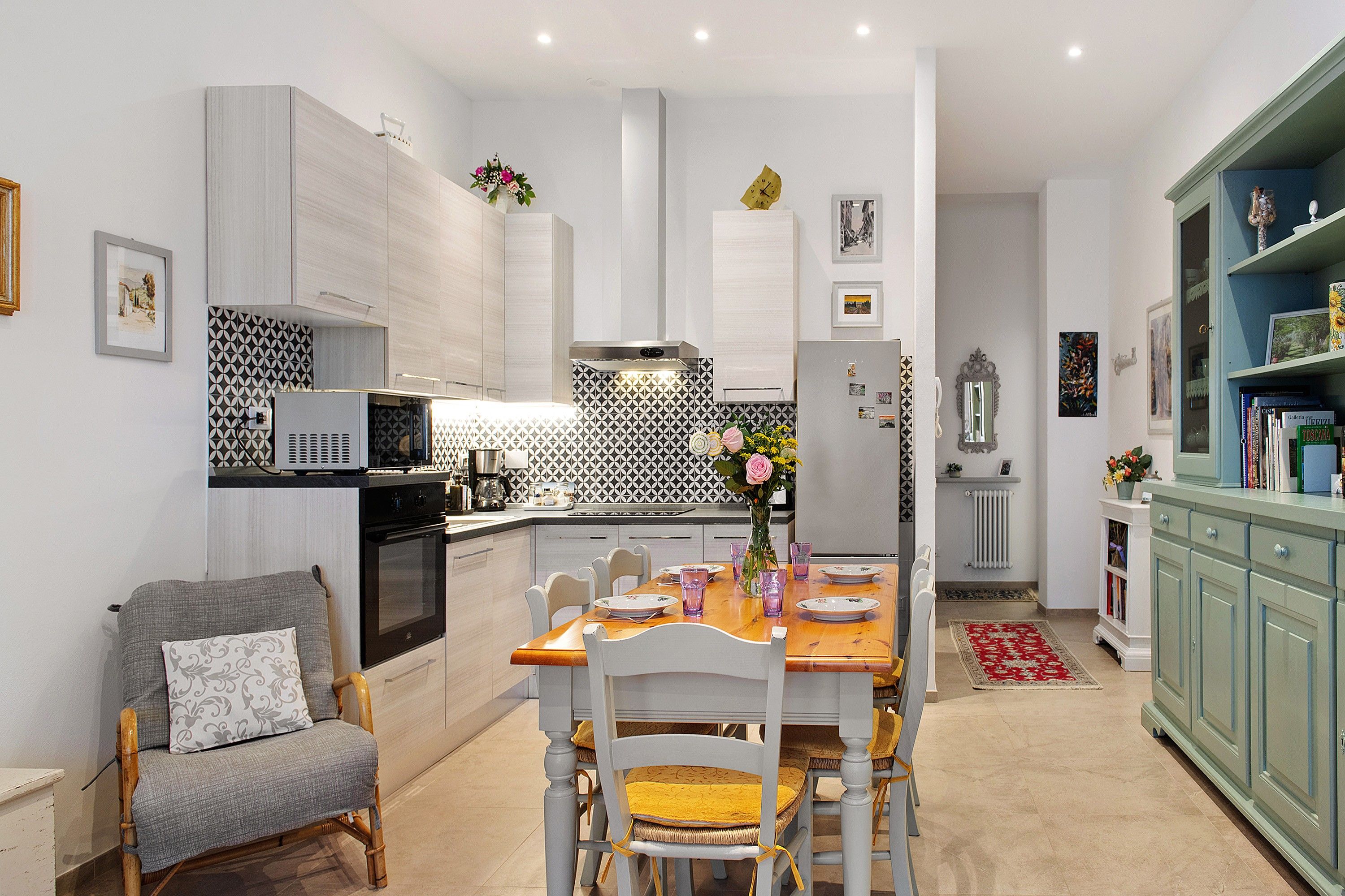 A modern kitchen with white cabinetry, a dining table set for four, and a bookshelf with books and decorative items.