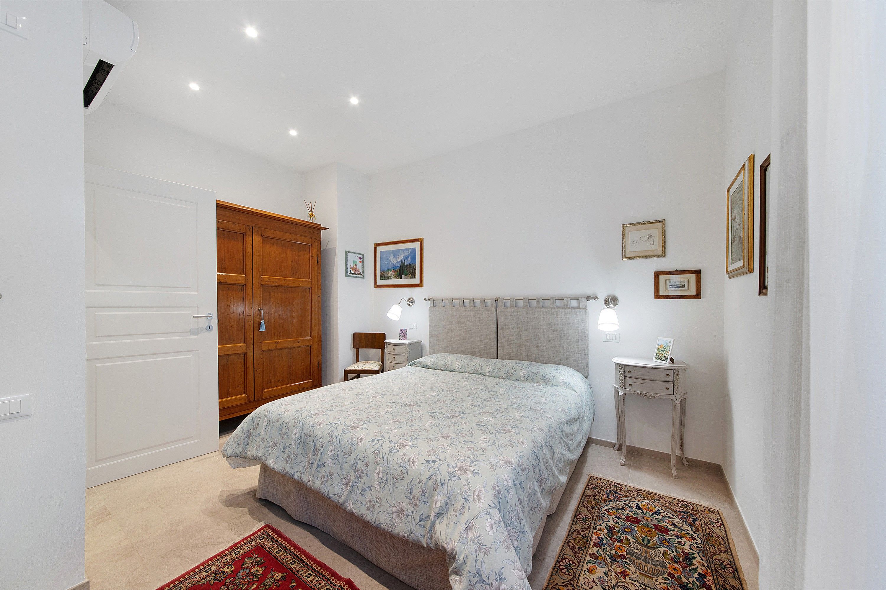 A bedroom with a bed, a wardrobe, a bedside table with a lamp, and a rug.