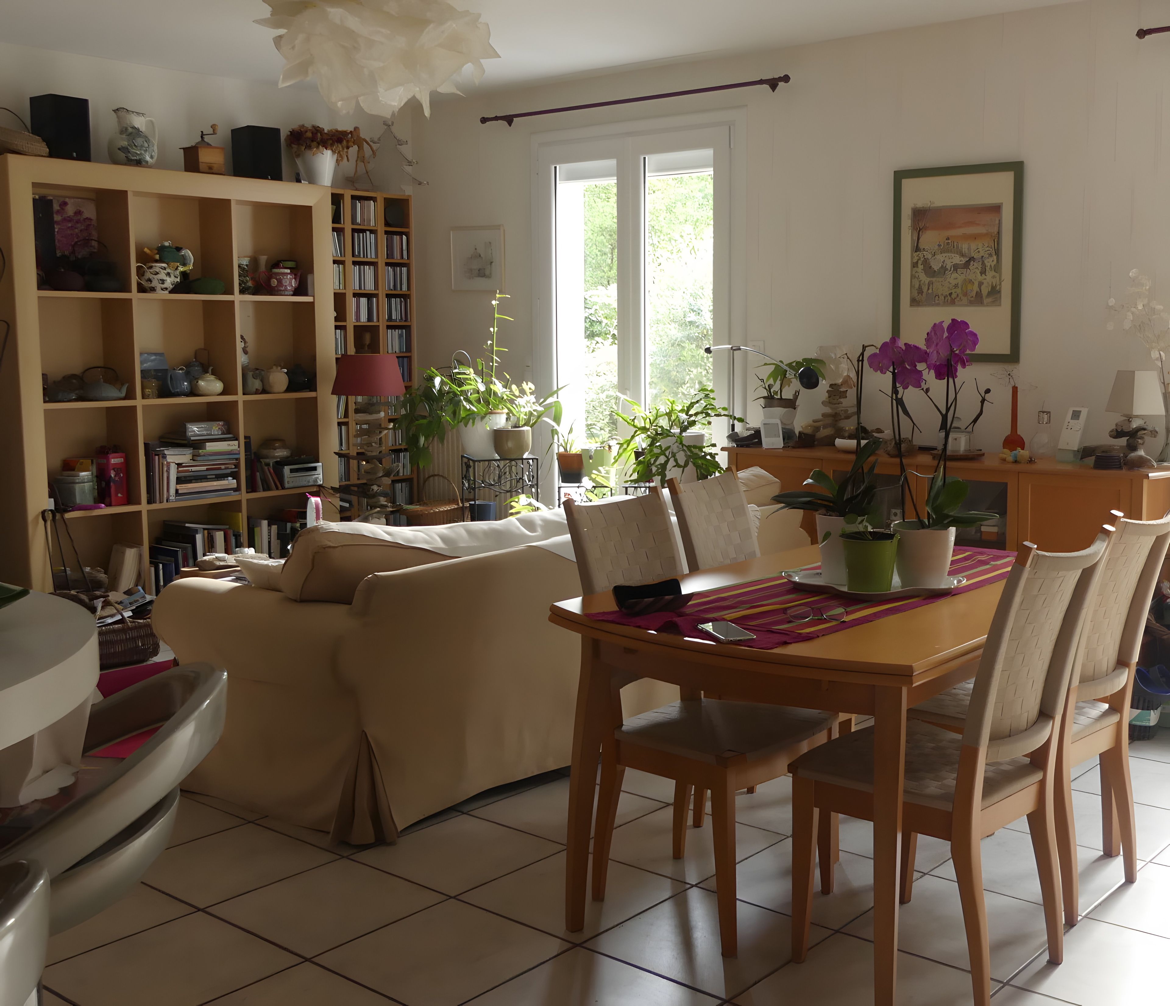 Ein Wohnzimmer mit einer Couch, Esstisch, Stühlen, einem Bücherregal und verschiedenen Dekorationselementen.