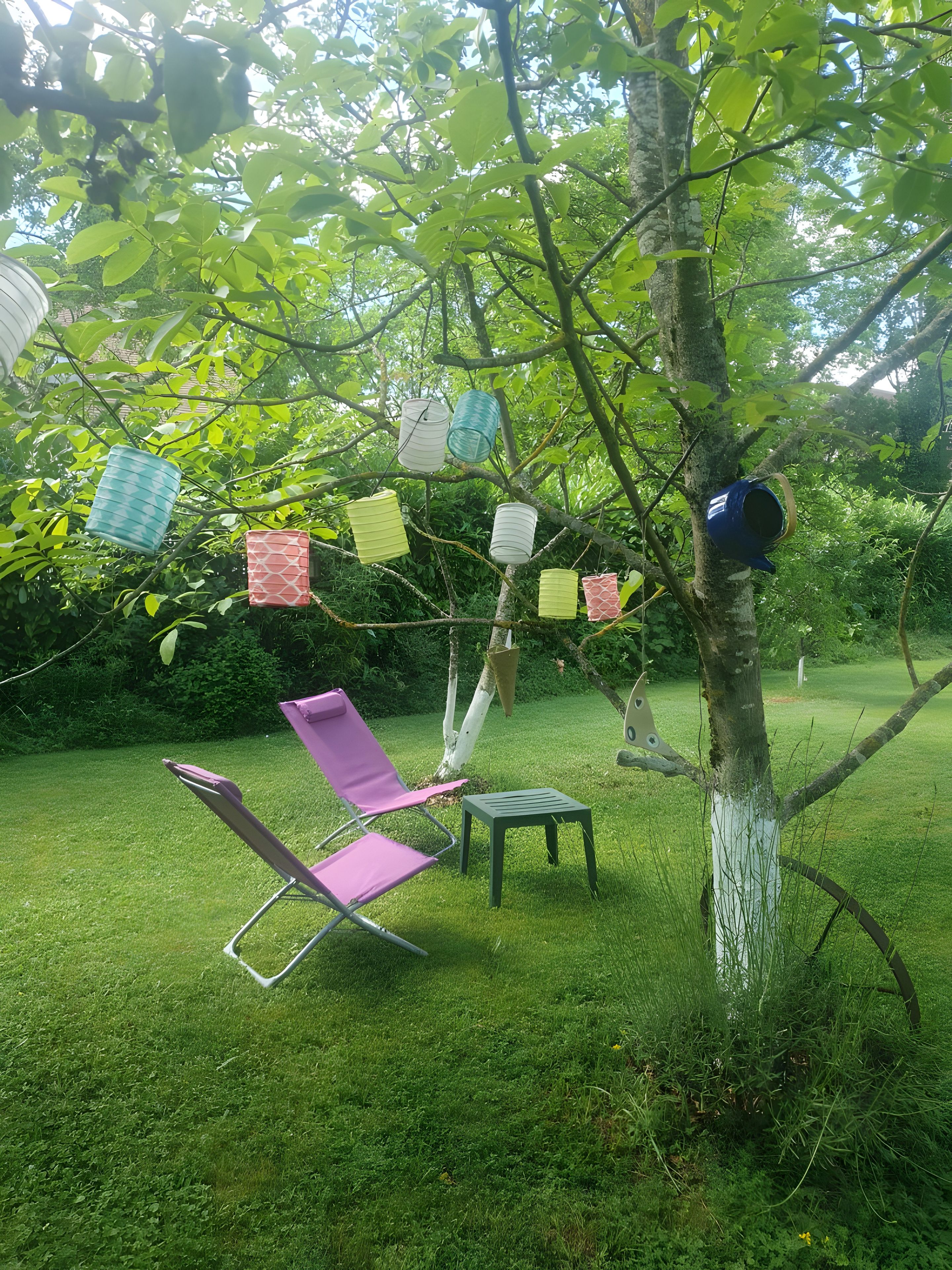 Ein Baum mit hängenden Laternen und einem rosa Stuhl auf einer Rasenfläche.