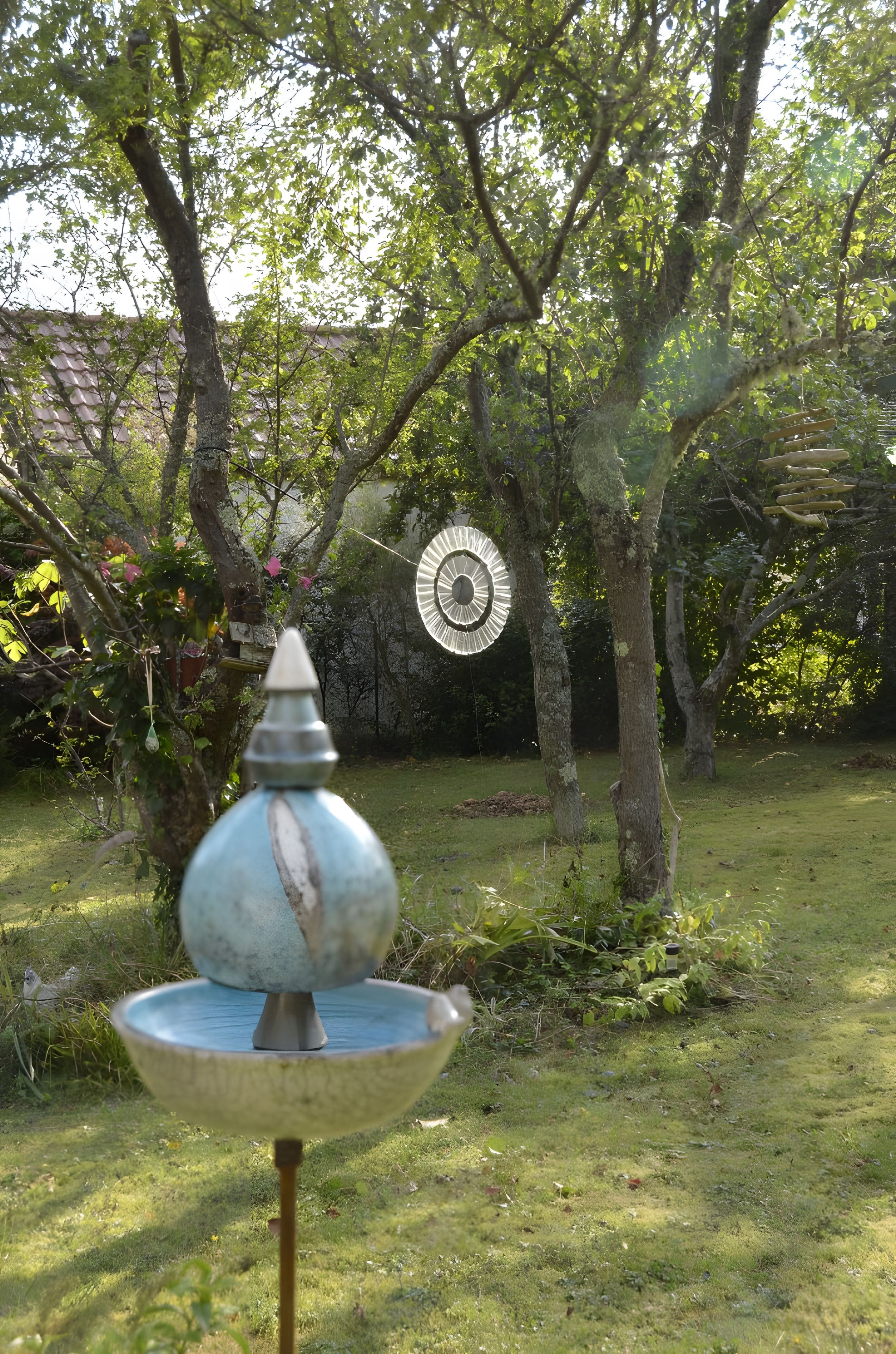 Un giardino con una vasca per uccelli e una scultura circolare in metallo.