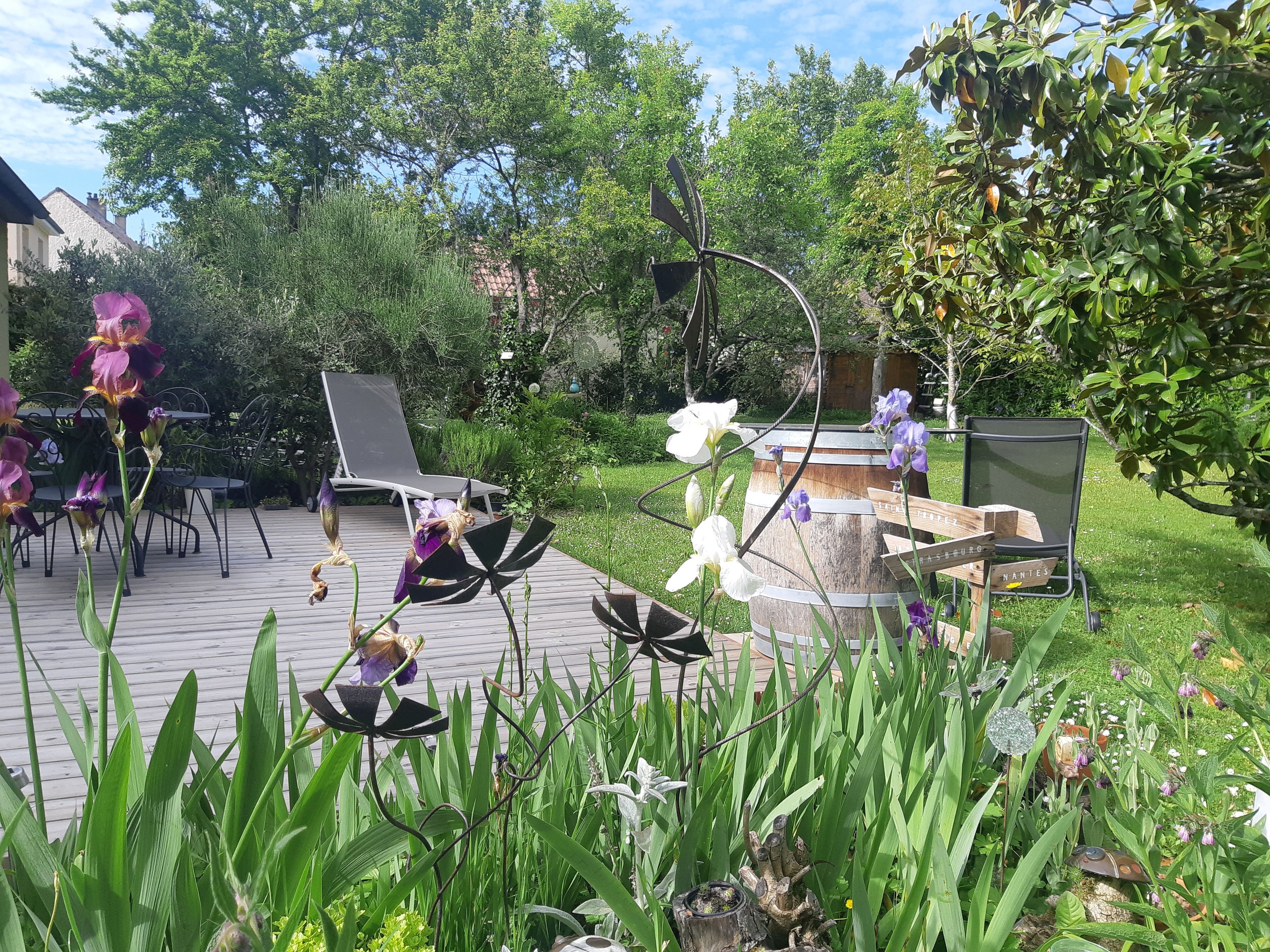 Een tuinpatio met tuinmeubilair, een houten vat en verschillende planten.